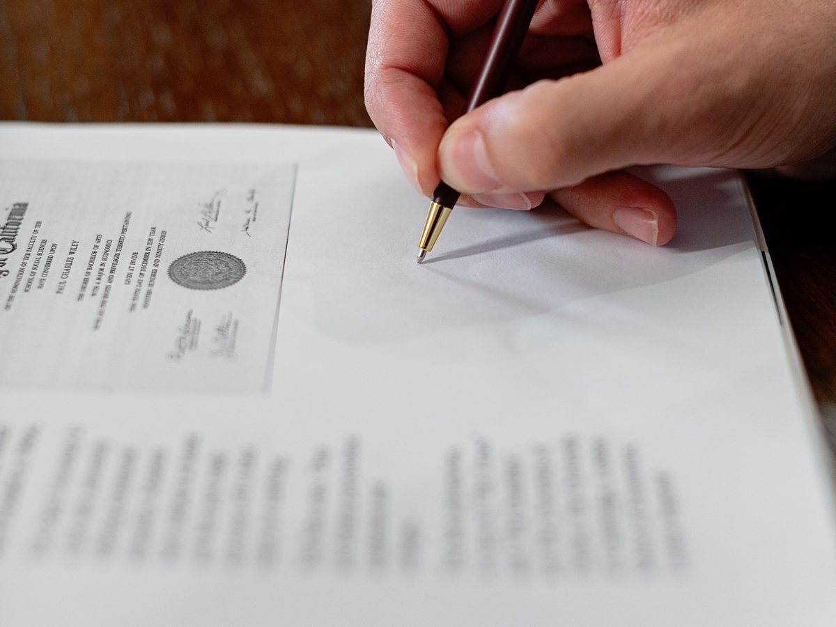 Close-up of a hand signing an official sealed document with a pen