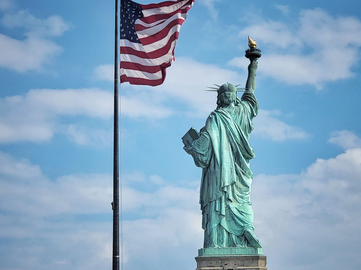 The Statue of Liberty beside a United States flag against a blue sky